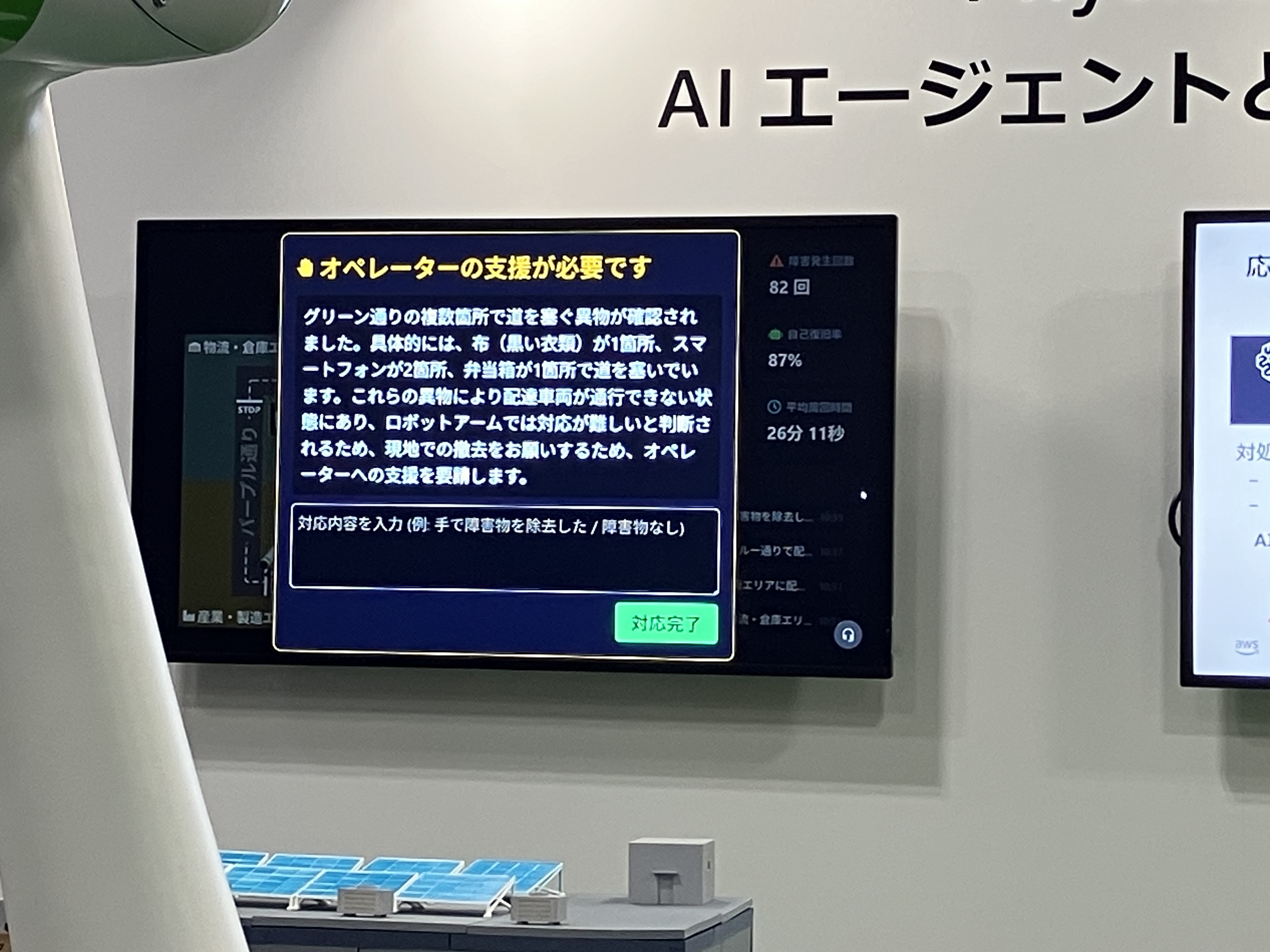 スクリーンに表示されたAIエージェントの報告。「オペレーターの支援が必要です」布・スマートフォン2箇所が道を塞いでおり、ロボットアームでは対応が難しいと判断、オペレーターへ支援を要請