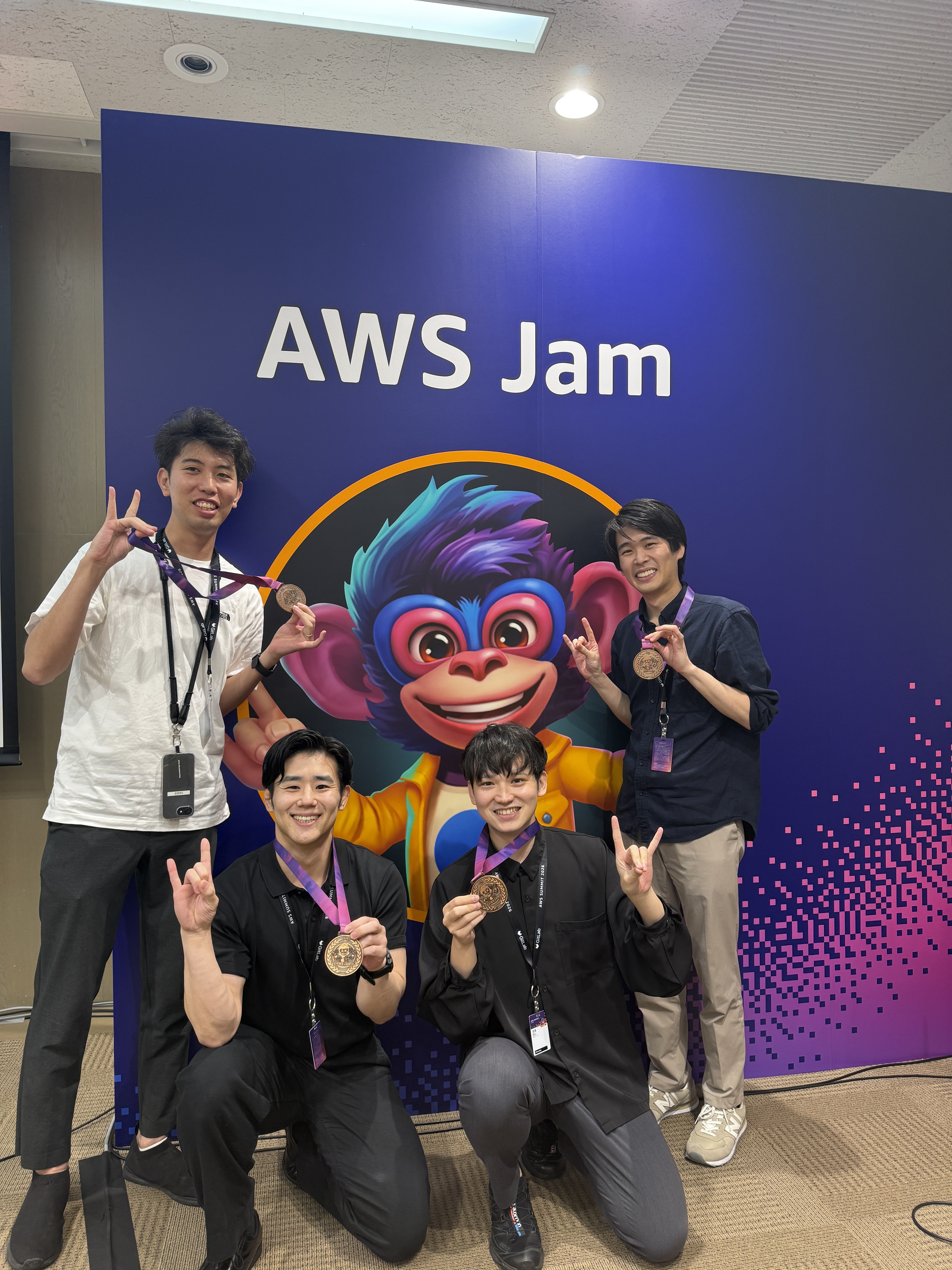 AWS Jam のロゴを背景に、3位チームのメンバーがメダルを手に記念撮影
